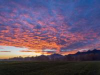 Rötlich leuchtende Haufenwolken fächern am Morgenhimmel über den Bergen